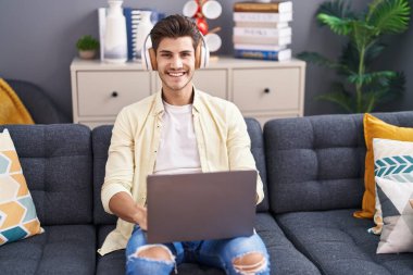 Genç İspanyol adam evdeki kanepede oturmuş müzik dinliyor.