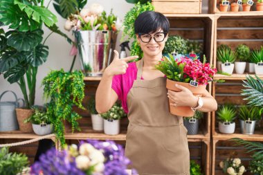 Young asian woman with short hair working at florist shop holding plant smiling happy pointing with hand and finger 