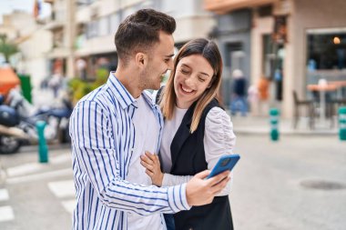 Man and woman couple hugging each other using smartphone at street