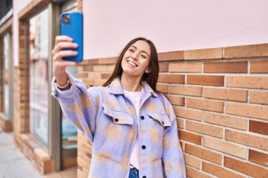 Genç ve güzel İspanyol kadın gülümsüyor. Kendine güveni tam. Sokakta akıllı telefonun yanında selfie çekiyor.