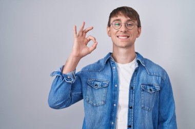 Caucasian blond man standing wearing glasses smiling positive doing ok sign with hand and fingers. successful expression. 