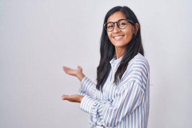 Young hispanic woman wearing glasses inviting to enter smiling natural with open hand 