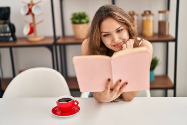 Genç, güzel İspanyol kadın kitap okuyor ve evde kahve içiyor.