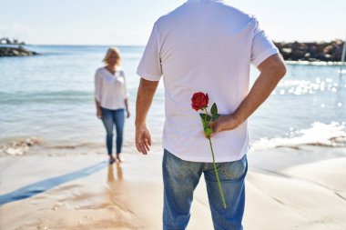 Middle age man and woman couple surprise with flower on back at seaside