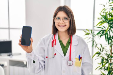 Genç İspanyol doktor kadın akıllı telefon ekranı gösteriyor. Pozitif ve mutlu görünüyor. Kendine güvenen bir gülümsemeyle dişlerini gösteriyor. 