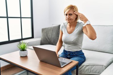 Orta yaşlı sarışın bir kadın evde dizüstü bilgisayar kullanıyor ve kendini vuruyor. Elini ve parmaklarını silah gibi kullanıyor. İntihar jesti.. 