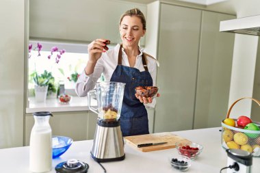 Genç sarışın kadın gülümsüyor. Mutfaktaki mikserin üzerine kendinden emin tarihler döküyor.