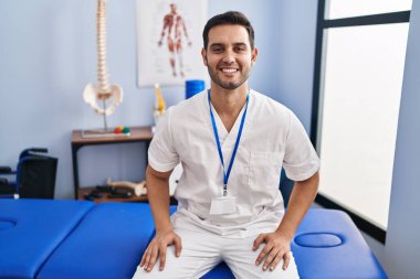 Sakallı, sakallı, mutlu ve havalı bir gülümsemeyle ağrı kesici kliniğinde çalışan genç bir İspanyol. şanslı kişi. 