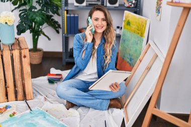 Akıllı telefondan konuşan genç kadın sanatçı resim stüdyosunda resim çekiyor.