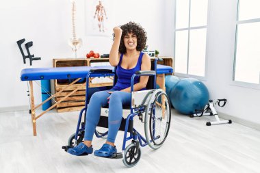Fizyoterapi kliniğinde tekerlekli sandalyede oturan genç bir kadın öfkeyle bağırırken kızgın ve kızgın bir şekilde yumruğunu kaldırıyor. öfke ve agresif konsept. 