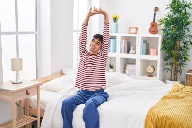 Young hispanic man waking up stretching arms at bedroom
