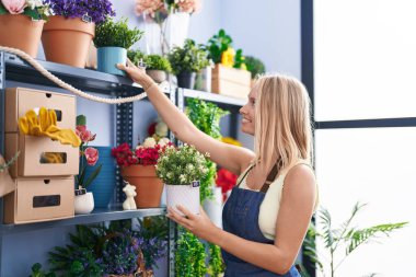 Çiçekçide çiçek tutan, gülümseyen genç sarışın kadın.