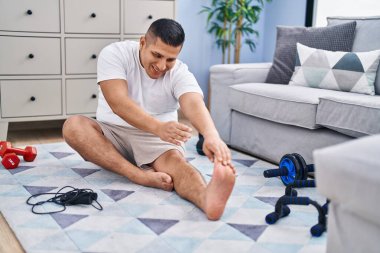 Genç latin adam gülümsüyor evde kendine güvenen esneme bacağı