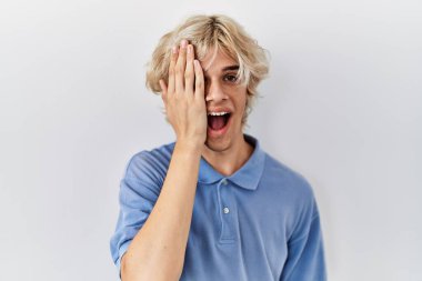 Genç modern adam izole edilmiş arka planda duruyor. Bir gözünü eliyle kapatıyor. Yüzünde kendine güvenen bir gülümseme ve şaşırtıcı bir duygu var.. 