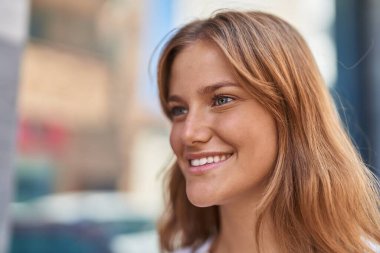 Young blonde girl smiling confident looking to the side at street
