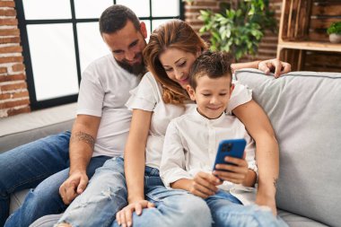 Family using smartphone hugging each other sitting on sofa at home