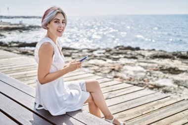 Kumsaldaki bankta oturan beyaz bir kız akıllı telefon kullanıyor..