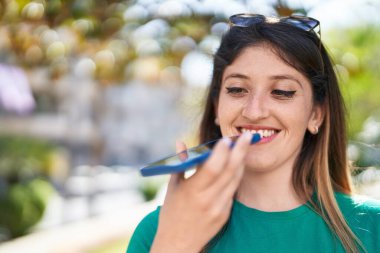 Genç İspanyol kadın gülümsüyor. Parktaki akıllı telefondan konuşuyor.