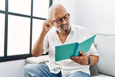 Kıdemli gri saçlı adam evde kendinden emin bir şekilde kitap okuyor.