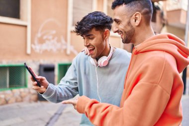 İki erkek caddede birbirlerine akıllı telefon kullanarak sarılıyorlar.
