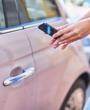 Young beautiful hispanic woman opening car door with smartphone at street