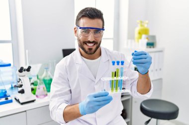 Laboratuvarda deney tüpü tutan bilim adamı üniforması giyen İspanyol genç adam.