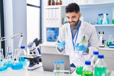 Young hispanic man wearing scientist uniform having video call at laboratory