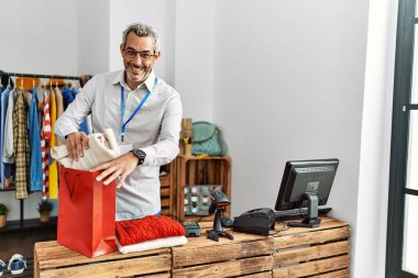 Orta yaşlı, gri saçlı bir dükkan asistanı giyim mağazasından alışveriş yapmaya hazırlanıyor.