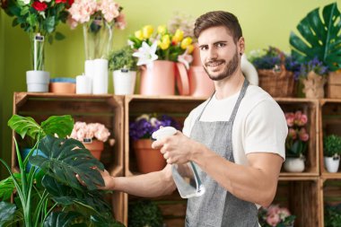 Genç beyaz erkek çiçekçi çiçekçide dağıtıcı sulama bitkisini kullanıyor.