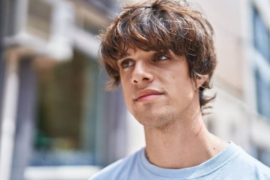 Sokakta ciddi bir ifadeyle yan tarafa bakan genç sarışın adam.