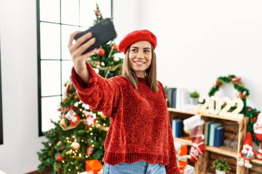 Genç İspanyol kız akıllı telefonun yanında selfie çekiyor. Noel ağacının yanında duruyor..