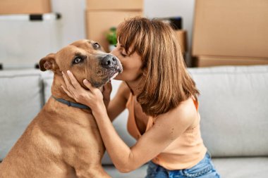 Beyaz bir kadın evdeki kanepede öpüşüyor ve köpeğe sarılıyor.