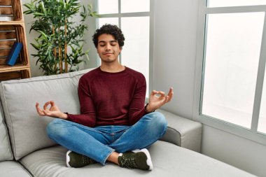 Genç İspanyol adam meditasyonu. Evdeki kanepede yoga yapıyor..