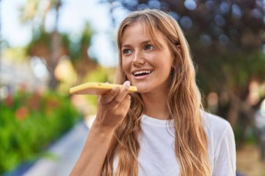 Young blonde girl smiling confident talking on the smartphone at park