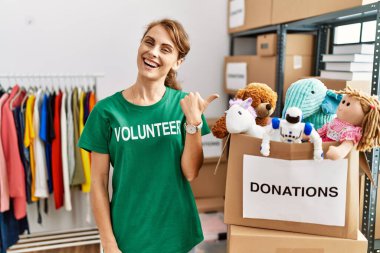 Bağışta gönüllü tişört giyen beyaz güzel bir kadın arka tarafı işaret ediyor. El ve baş parmakları havada, kendinden emin gülümsüyor. 