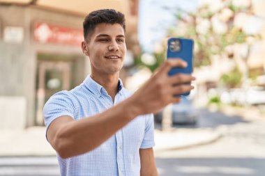 Genç İspanyol adam gülümsüyor. Sokakta akıllı telefonun yanında özçekim yapıyor.