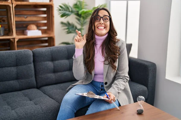 Young Brunette Woman Working Consultation Office Gesturing Finger Crossed Smiling — Fotografia de Stock