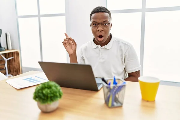 Young African Man Working Office Using Computer Laptop Surprised Pointing — Φωτογραφία Αρχείου