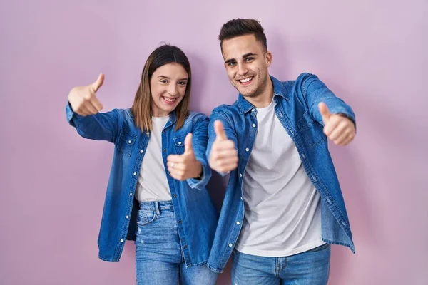 Young Hispanic Couple Standing Pink Background Approving Doing Positive Gesture — Stockfoto