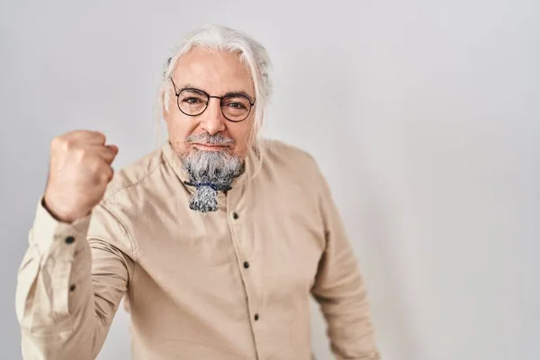 Middle age man with grey hair standing over isolated background angry and mad raising fist frustrated and furious while shouting with anger. rage and aggressive concept.