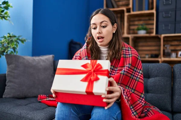 Young hispanic woman opening gift box afraid and shocked with surprise and amazed expression, fear and excited face.