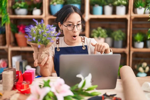Young hispanic woman working at florist shop doing video call pointing down with fingers showing advertisement, surprised face and open mouth