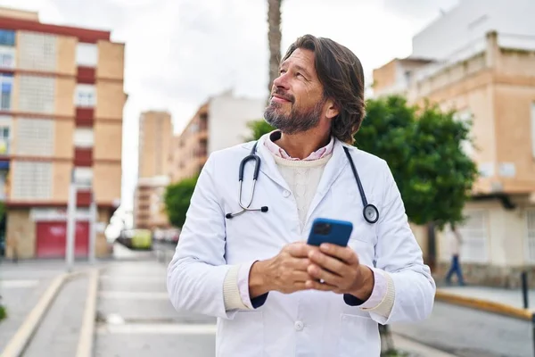 中年男性医師笑顔自信を持って使用してスマートフォンでストリート — ストック写真