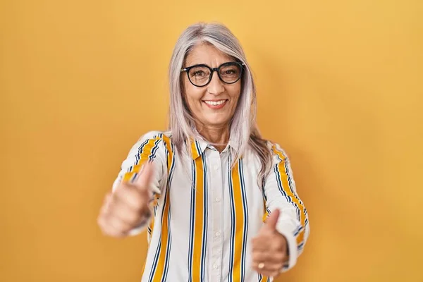 Kobieta Średnim Wieku Siwymi Włosami Stojąca Żółtym Tle Okularach Zatwierdzających — Zdjęcie stockowe