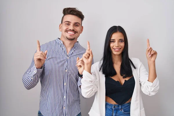 Young Hispanic Couple Standing White Background Smiling Amazed Surprised Pointing — Stockfoto