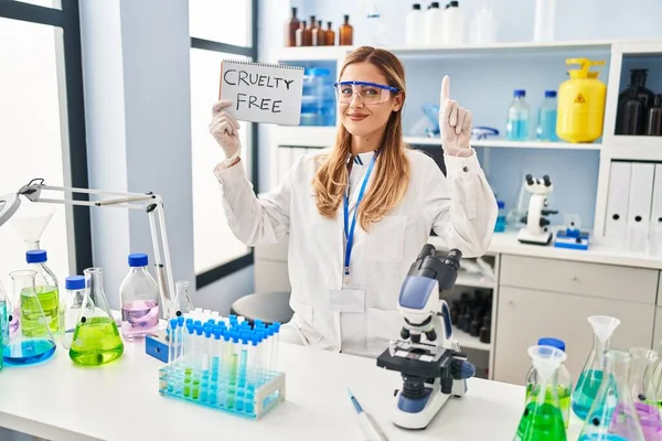 Young blonde scientist woman working on cruelty free laboratory surprised with an idea or question pointing finger with happy face, number one