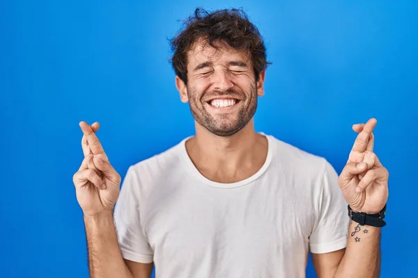 Jovem Hispânico Sobre Fundo Azul Gesto Dedo Cruzado Sorrindo Com — Fotografia de Stock