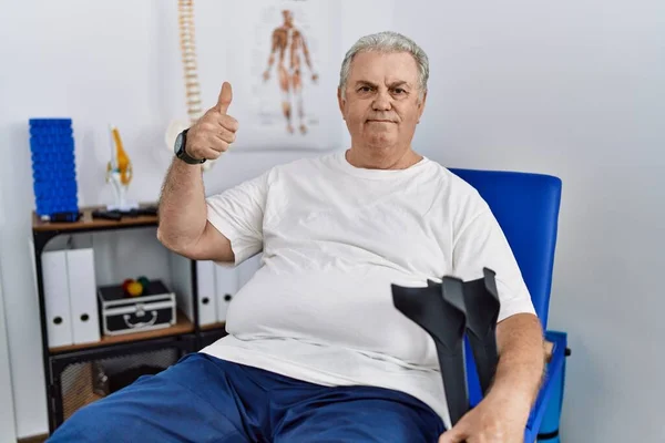 Homem Caucasiano Sênior Clínica Fisioterapia Segurando Muletas Fazendo Polegares Felizes — Fotografia de Stock