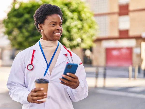 stock image African american woman wearing doctor uniform using smartphone drinking coffee at park