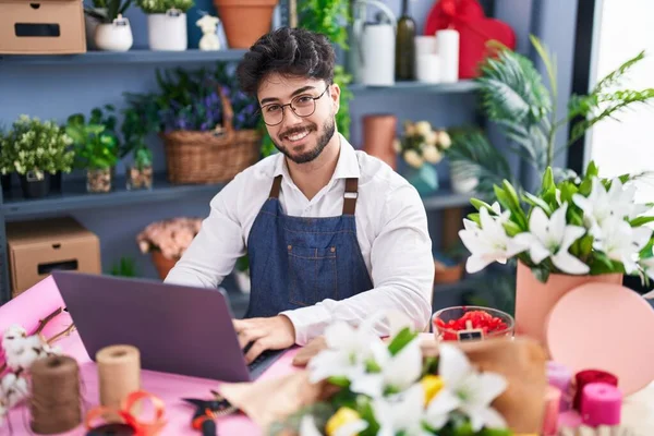 Young hispanic man florist smiling confident using laptop at florist shop